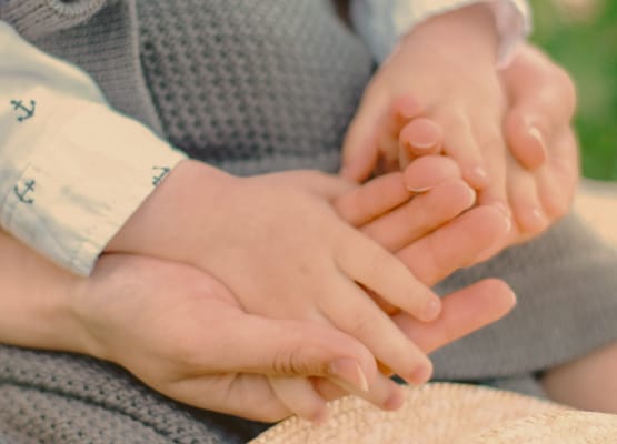 Mamma è seduta con il bambino piccolo sulle gambe e gli tiene le mani (fotografia: Kira Ikonnikova su Unsplash)